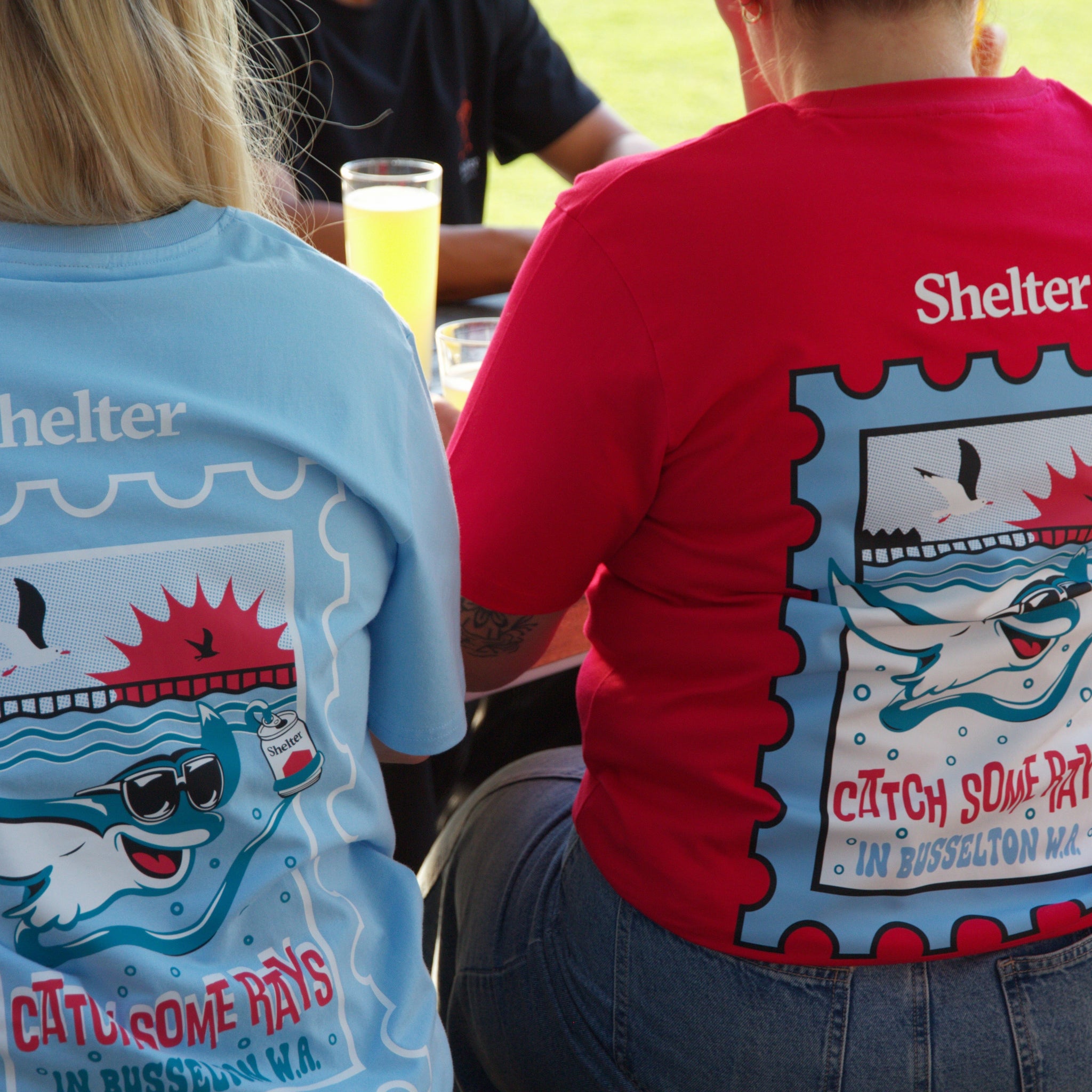 Two Shelter workers outside wearing Catch some rays tee's in crimson and sky